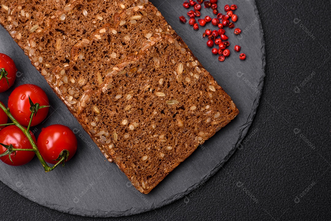 Delicioso pão integral fresco e crocante com sementes e grãos cortados em fatias sobre um fundo escuro de concreto