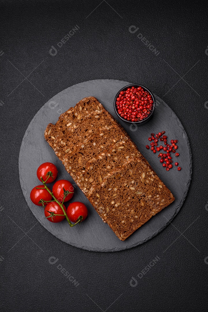 Delicioso pão integral fresco e crocante com sementes e grãos cortados em fatias sobre um fundo escuro de concreto