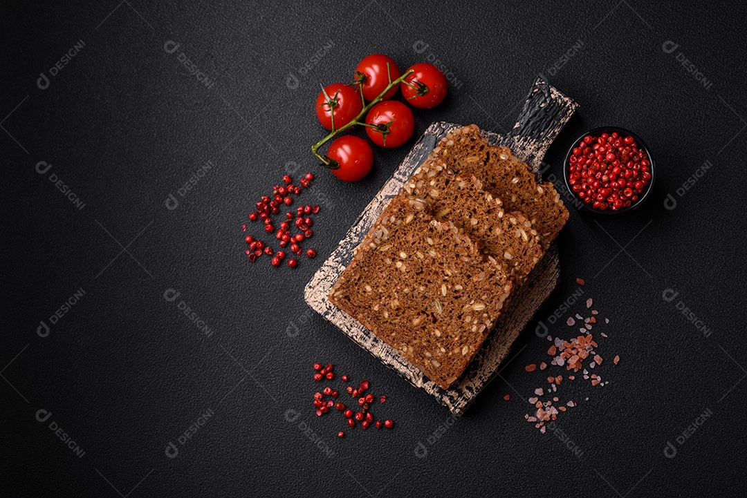 Delicioso pão integral fresco e crocante com sementes e grãos cortados em fatias sobre um fundo escuro de concreto