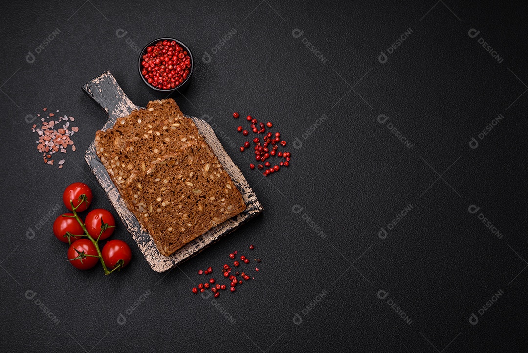 Delicioso pão integral fresco e crocante com sementes e grãos cortados em fatias sobre um fundo escuro de concreto