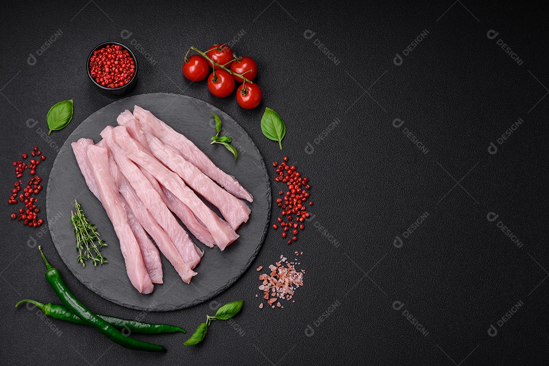 Filé de frango ou peru cru cortado em tiras com especiarias e ervas sobre um fundo escuro de concreto