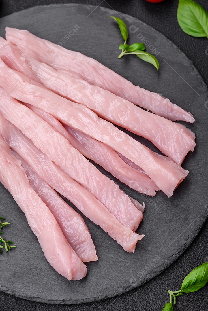 Filé de frango ou peru cru cortado em tiras com especiarias e ervas sobre um fundo escuro de concreto