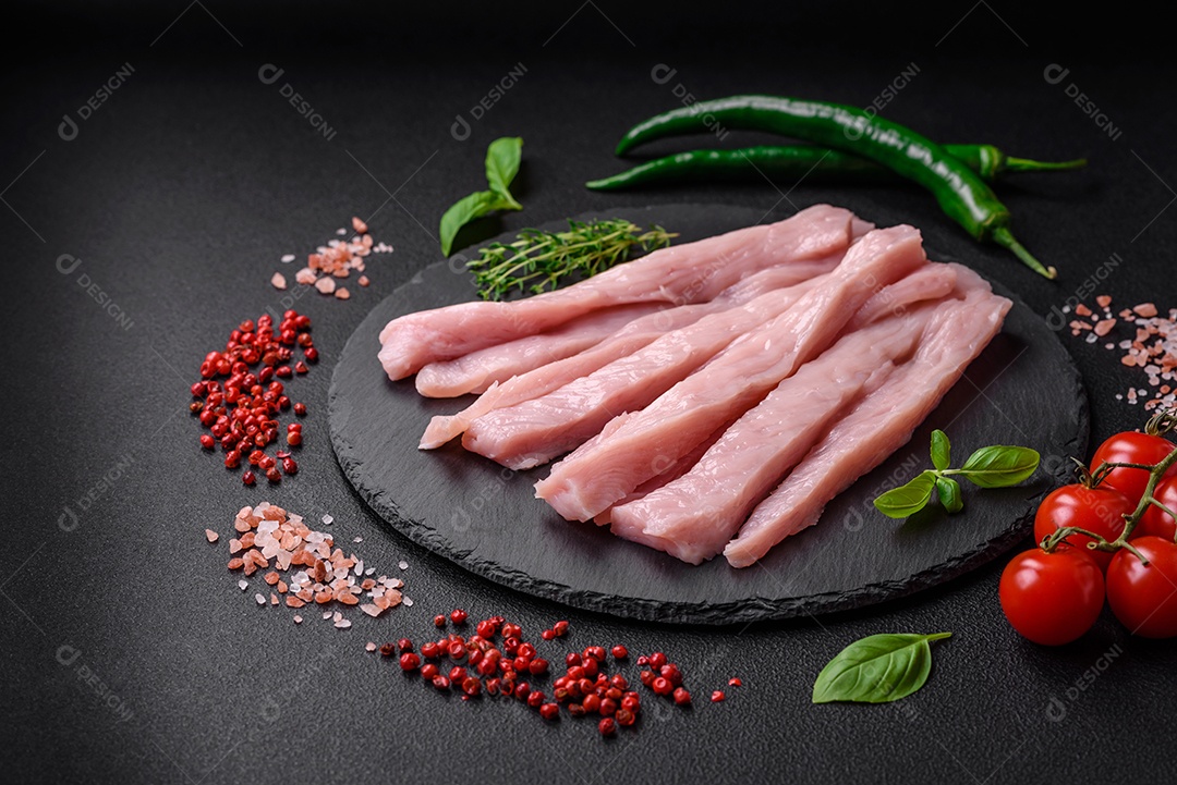 Filé de frango ou peru cru cortado em tiras com especiarias e ervas sobre um fundo escuro de concreto