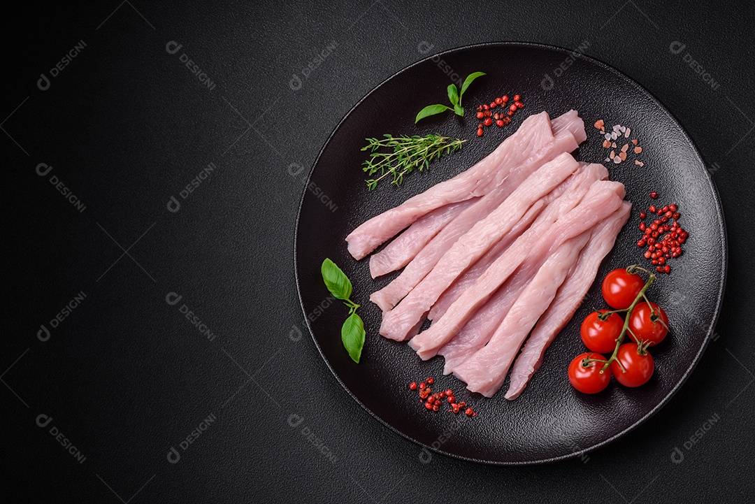 Filé de frango ou peru cru cortado em tiras com especiarias e ervas sobre um fundo escuro de concreto