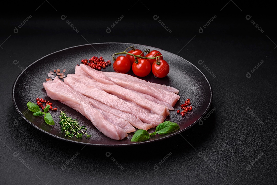 Filé de frango ou peru cru cortado em tiras com especiarias e ervas sobre um fundo escuro de concreto