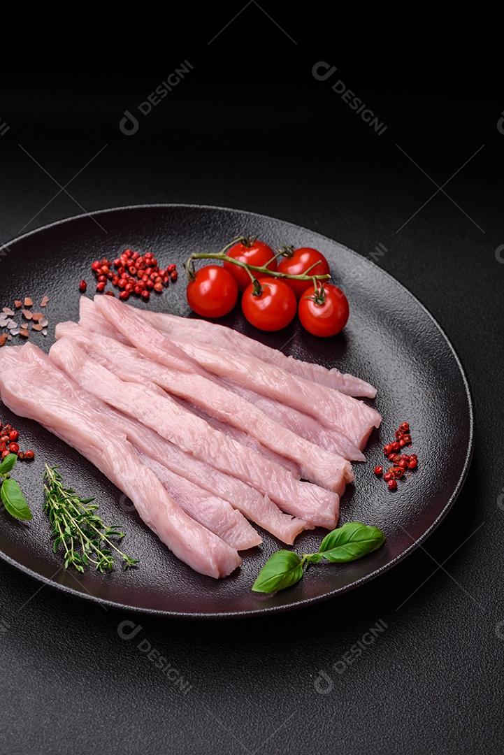 Filé de frango ou peru cru cortado em tiras com especiarias e ervas sobre um fundo escuro de concreto