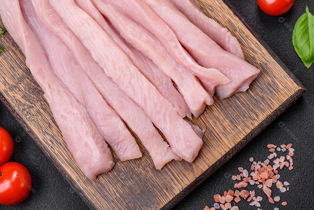 Filé de frango ou peru cru cortado em tiras com especiarias e ervas sobre um fundo escuro de concreto