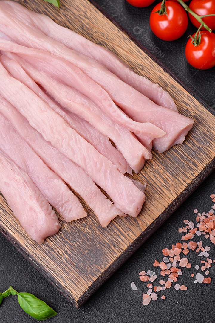 Filé de frango ou peru cru cortado em tiras com especiarias e ervas sobre um fundo escuro de concreto