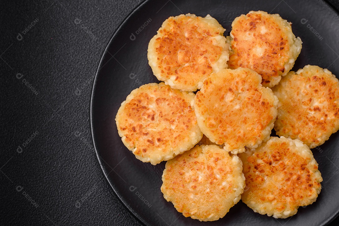 Deliciosos cheesecakes frescos com passas e baunilha em uma placa de cerâmica preta sobre um fundo escuro de concreto