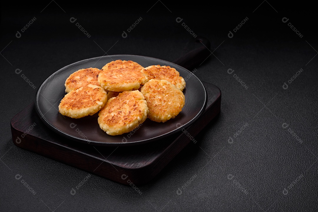 Deliciosos cheesecakes frescos com passas e baunilha em uma placa de cerâmica preta sobre um fundo escuro de concreto