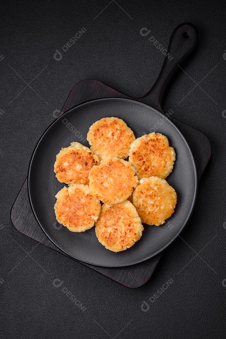 Deliciosos cheesecakes frescos com passas e baunilha em uma placa de cerâmica preta sobre um fundo escuro de concreto