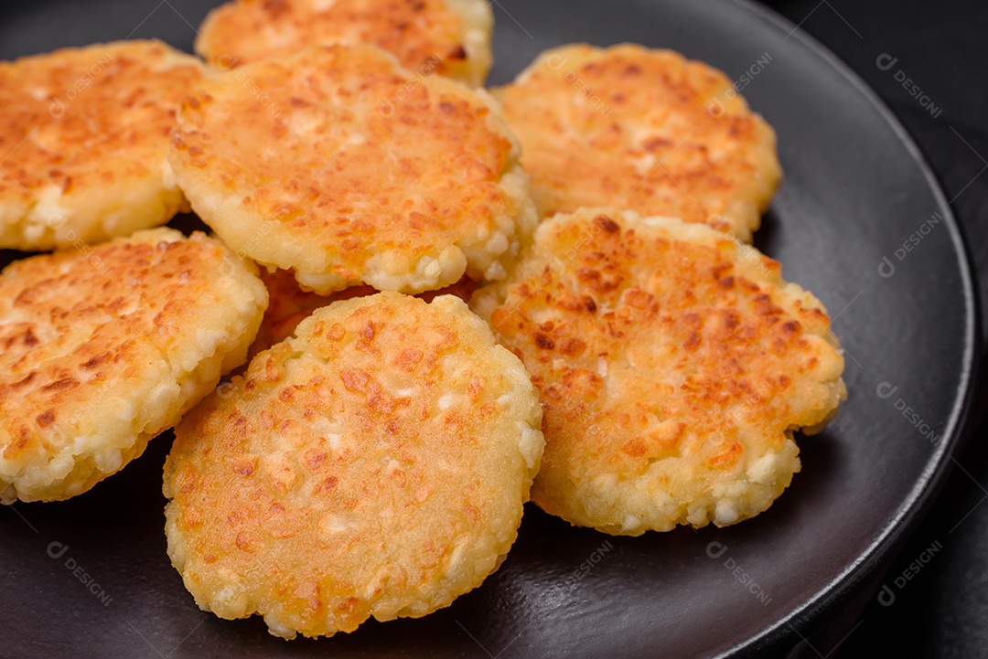 Deliciosos cheesecakes frescos com passas e baunilha em uma placa de cerâmica preta sobre um fundo escuro de concreto