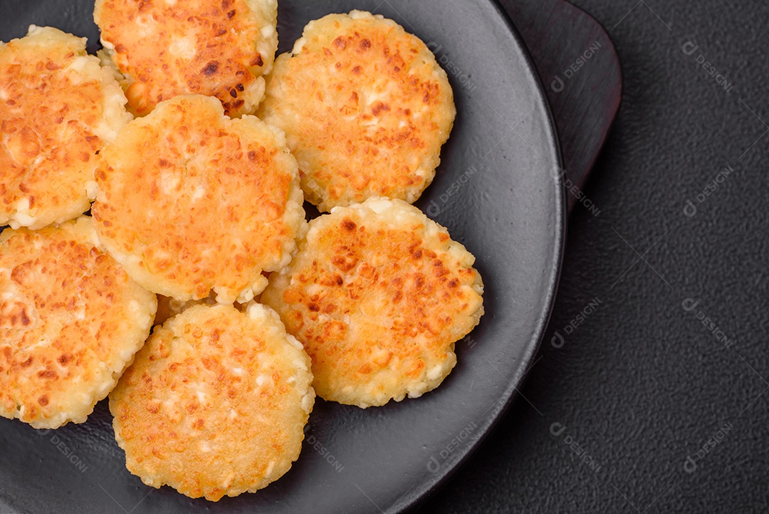 Deliciosos cheesecakes frescos com passas e baunilha em uma placa de cerâmica preta sobre um fundo escuro de concreto