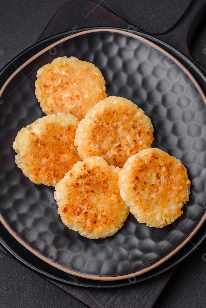 Deliciosos cheesecakes frescos com passas e baunilha em uma placa de cerâmica preta sobre um fundo escuro de concreto