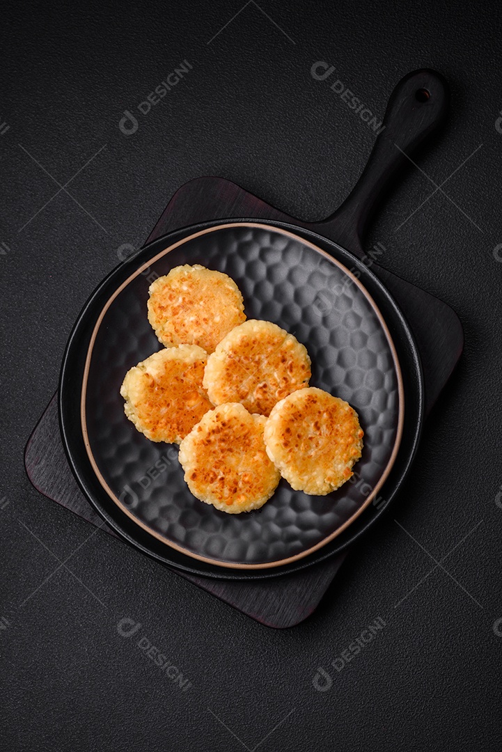 Deliciosos cheesecakes frescos com passas e baunilha em uma placa de cerâmica preta sobre um fundo escuro de concreto