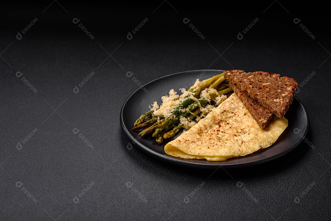 Delicioso café da manhã nutritivo composto por espargos, ovos mexidos, sal, especiarias e ervas sobre um fundo escuro de concreto