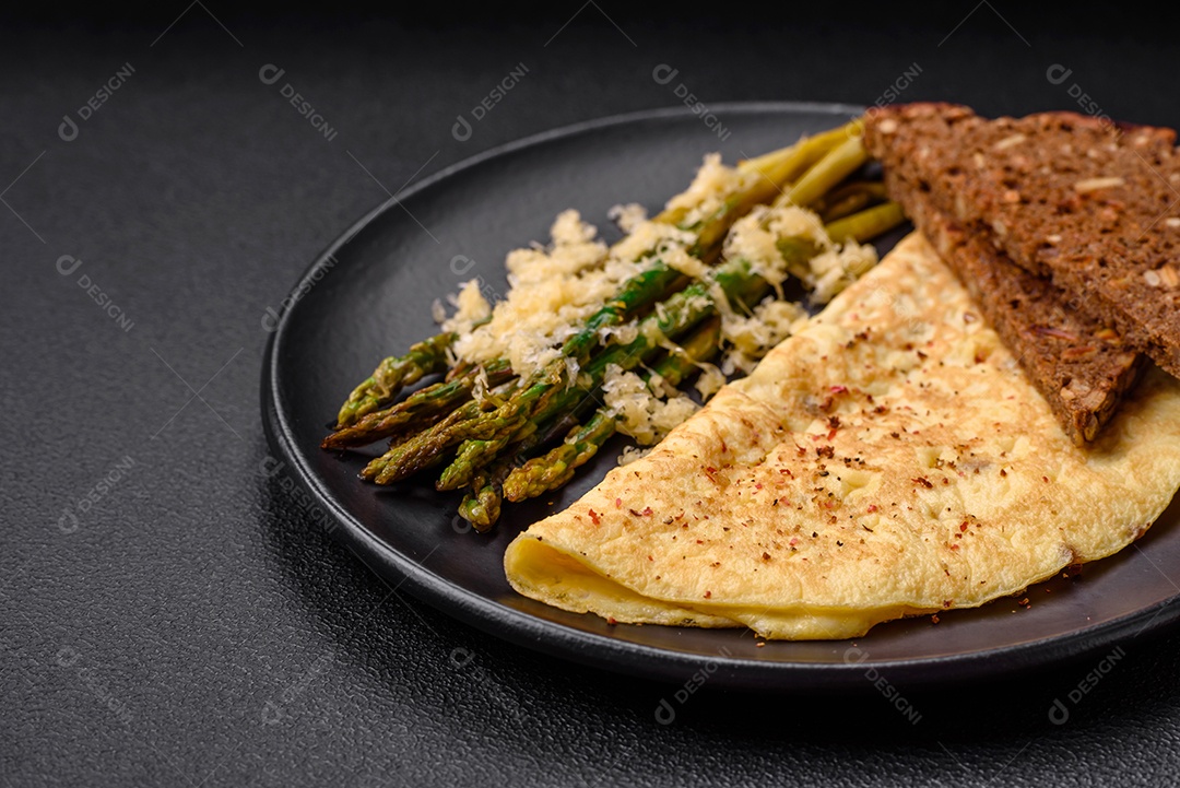 Delicioso café da manhã nutritivo composto por espargos, ovos mexidos, sal, especiarias e ervas sobre um fundo escuro de concreto