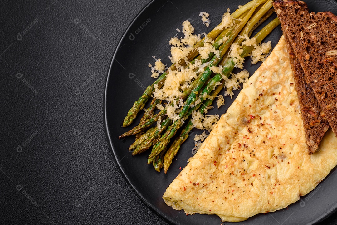 Delicioso café da manhã nutritivo composto por espargos, ovos mexidos, sal, especiarias e ervas sobre um fundo escuro de concreto