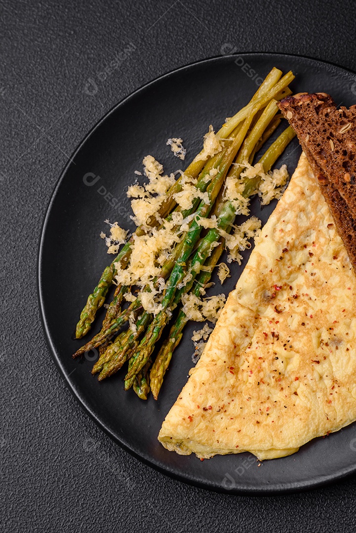 Delicioso café da manhã nutritivo composto por espargos, ovos mexidos, sal, especiarias e ervas sobre um fundo escuro de concreto