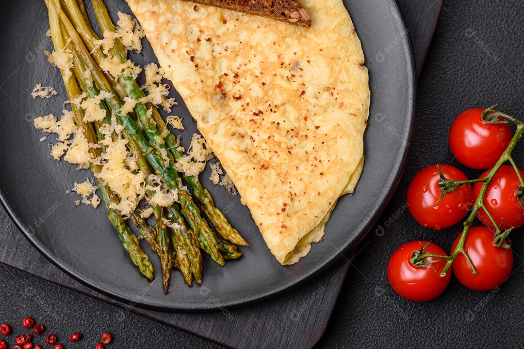 Delicioso café da manhã nutritivo composto por espargos, ovos mexidos, sal, especiarias e ervas sobre um fundo escuro de concreto