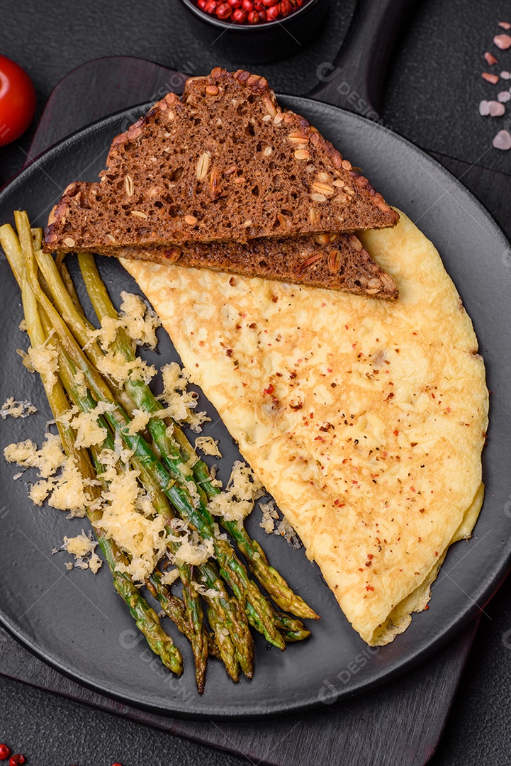 Delicioso café da manhã nutritivo composto por espargos, ovos mexidos, sal, especiarias e ervas sobre um fundo escuro de concreto