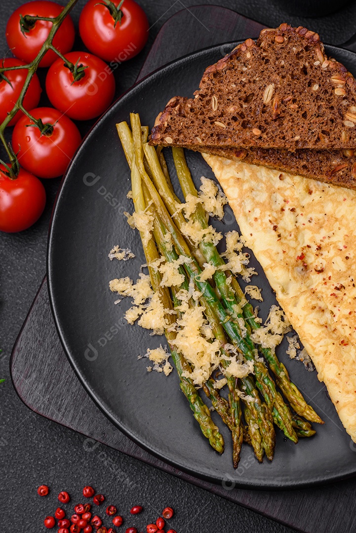 Delicioso café da manhã nutritivo composto por espargos, ovos mexidos, sal, especiarias e ervas sobre um fundo escuro de concreto