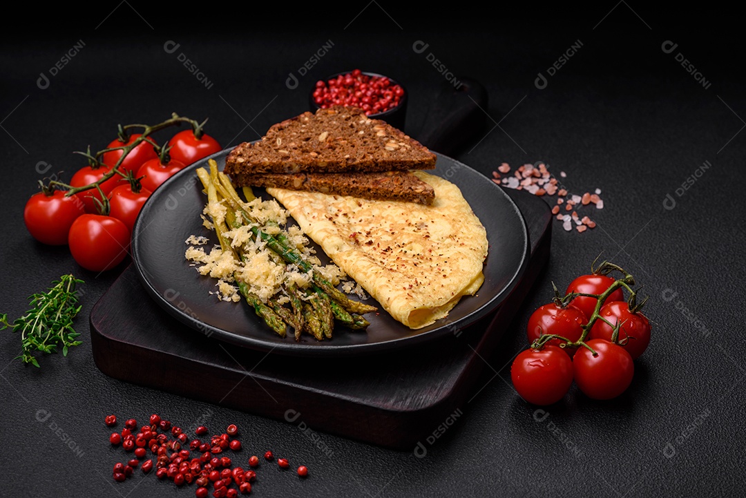 Delicioso café da manhã nutritivo composto por espargos, ovos mexidos, sal, especiarias e ervas sobre um fundo escuro de concreto