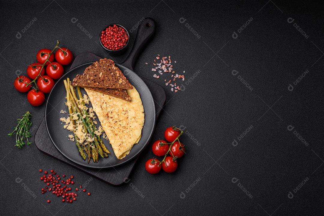 Delicioso café da manhã nutritivo composto por espargos, ovos mexidos, sal, especiarias e ervas sobre um fundo escuro de concreto