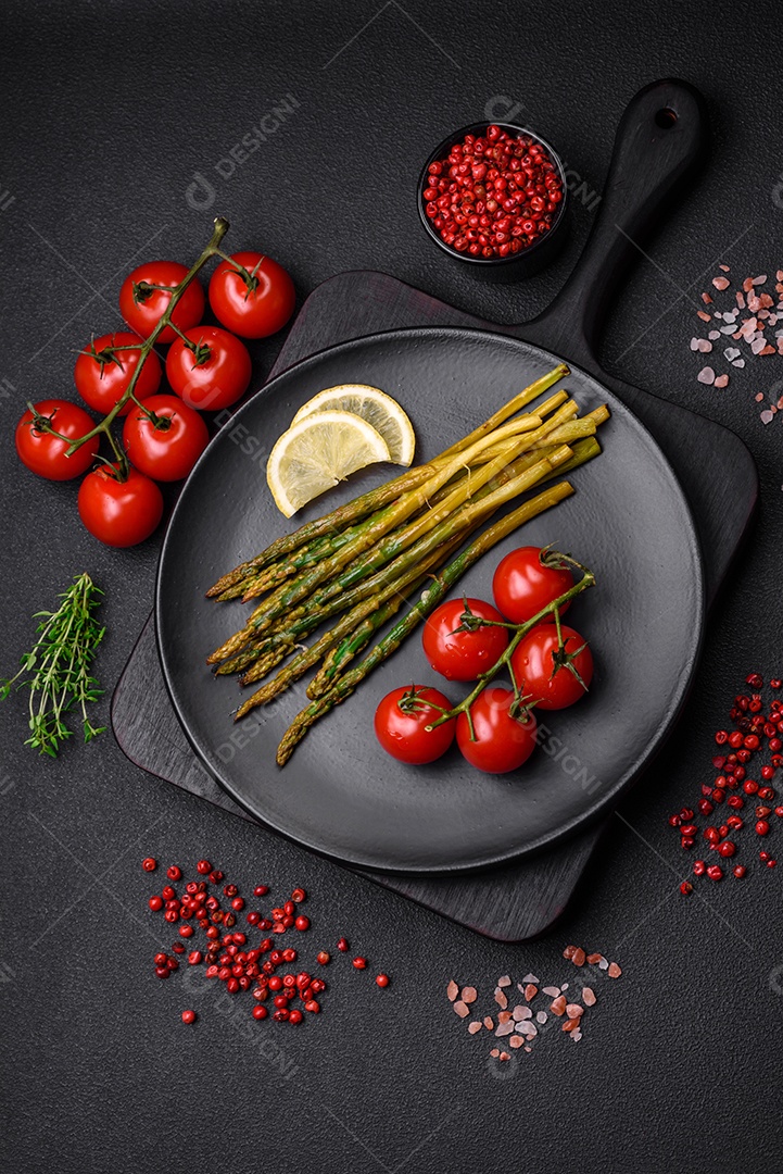 Delicioso café da manhã nutritivo composto por espargos, tomates, sal, especiarias e ervas sobre um fundo escuro de concreto