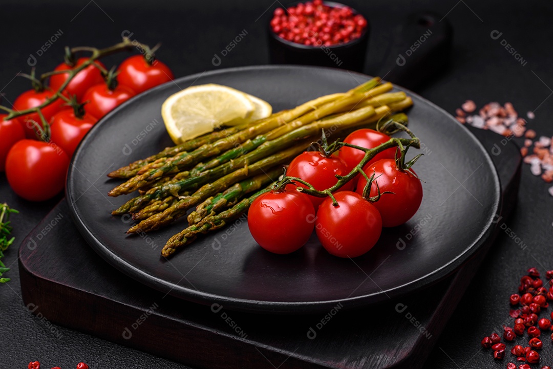 Delicioso café da manhã nutritivo composto por espargos, tomates, sal, especiarias e ervas sobre um fundo escuro de concreto