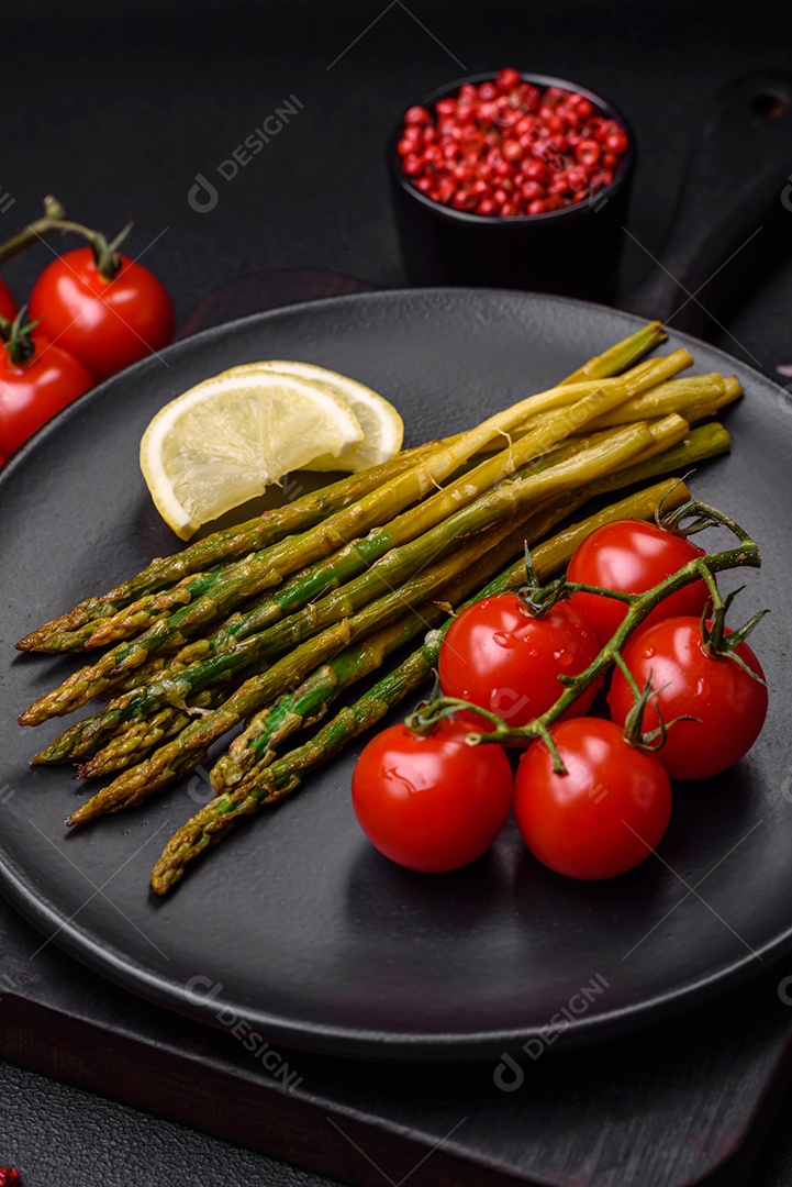 Delicioso café da manhã nutritivo composto por espargos, tomates, sal, especiarias e ervas sobre um fundo escuro de concreto