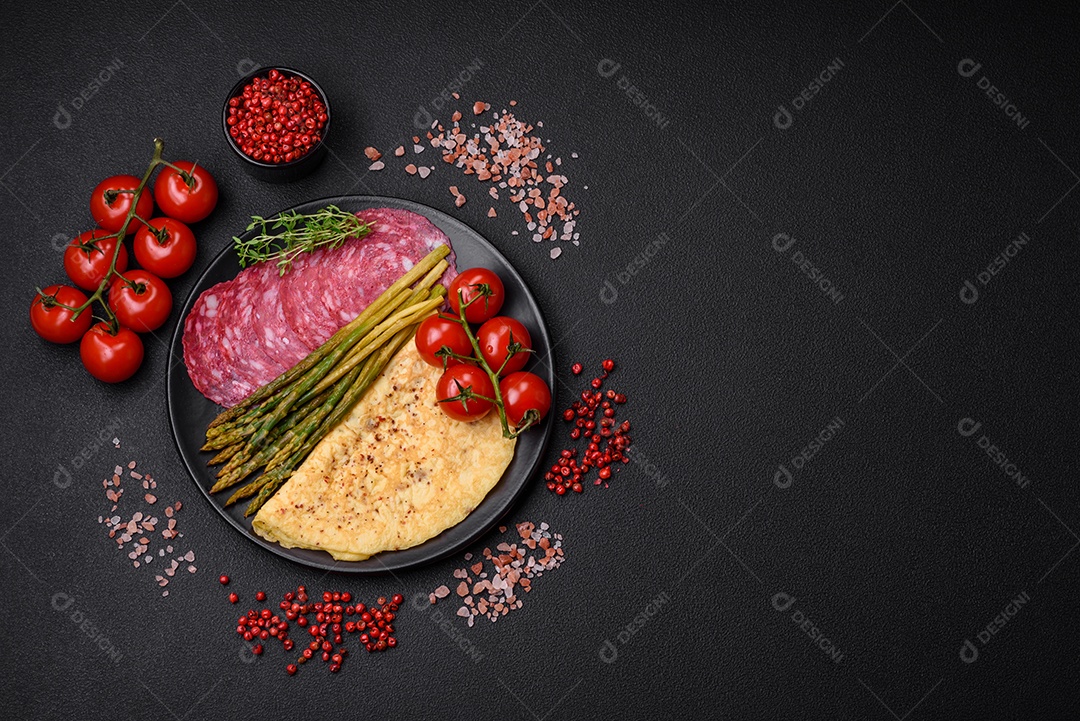 Delicioso café da manhã nutritivo composto por espargos, ovos mexidos, sal, especiarias e ervas sobre um fundo escuro de concreto