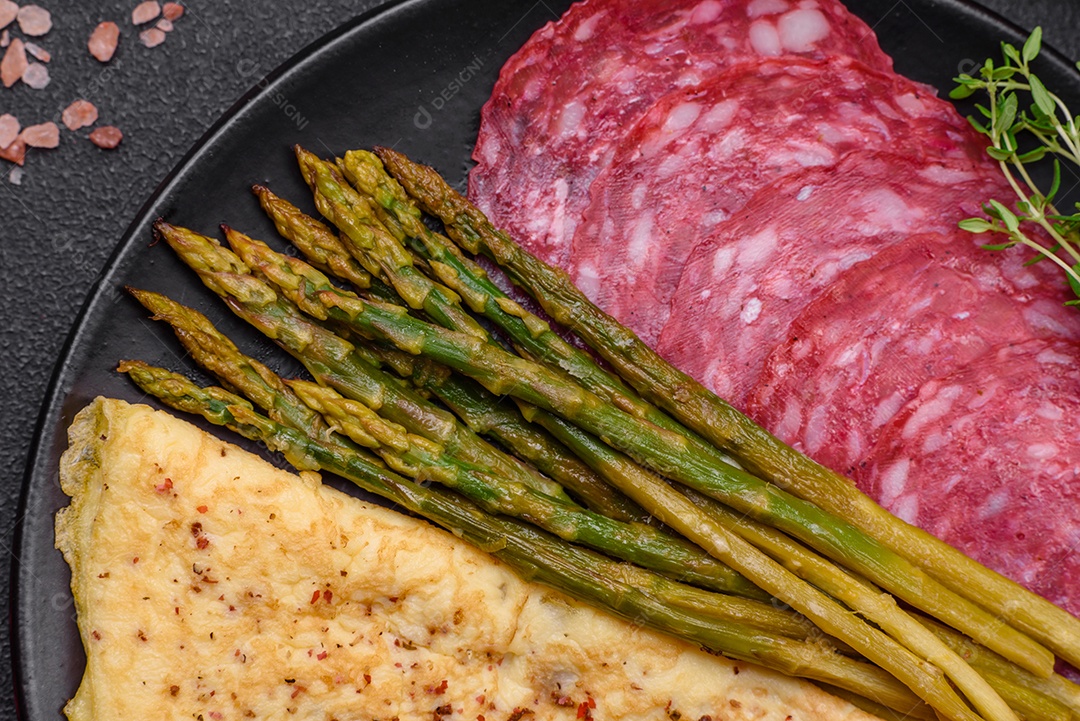 Delicioso café da manhã nutritivo composto por espargos, ovos mexidos, sal, especiarias e ervas sobre um fundo escuro de concreto