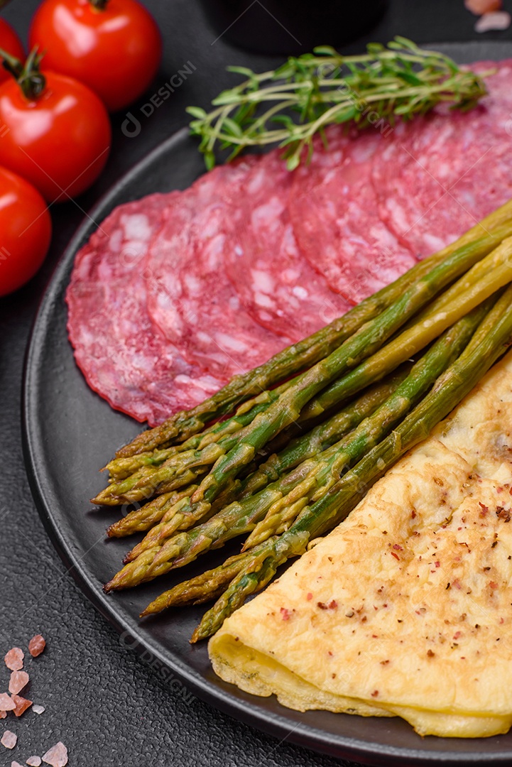 Delicioso café da manhã nutritivo composto por espargos, ovos mexidos, sal, especiarias e ervas sobre um fundo escuro de concreto