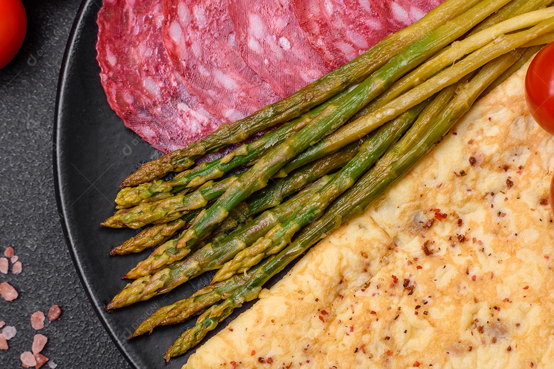 Delicioso café da manhã nutritivo composto por espargos, ovos mexidos, sal, especiarias e ervas sobre um fundo escuro de concreto