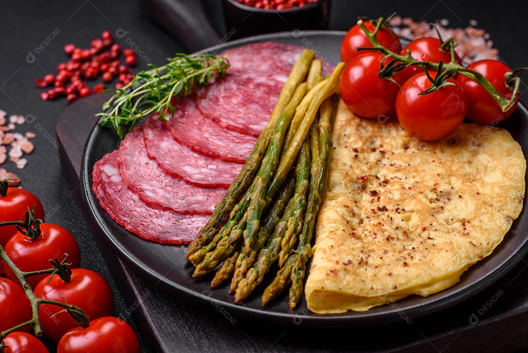 Delicioso café da manhã nutritivo composto por espargos, ovos mexidos, sal, especiarias e ervas sobre um fundo escuro de concreto