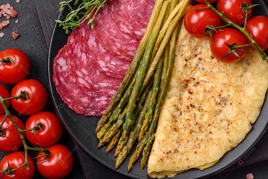 Delicioso café da manhã nutritivo composto por espargos, ovos mexidos, sal, especiarias e ervas sobre um fundo escuro de concreto