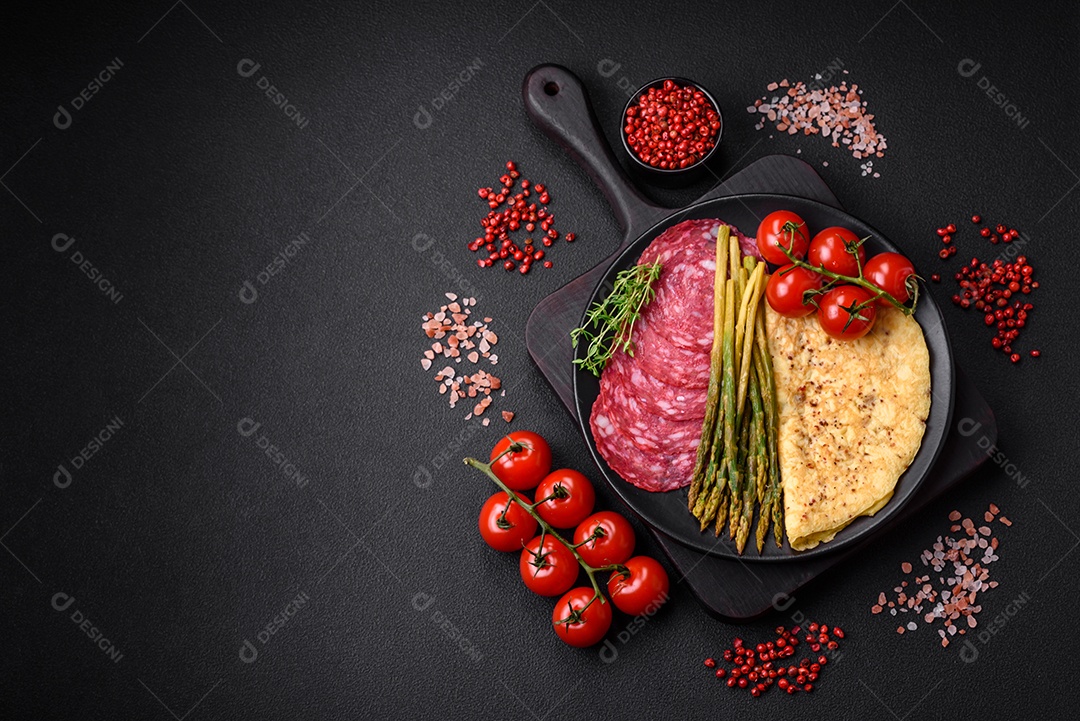 Delicioso café da manhã nutritivo composto por salsicha fatiada, espargos, sal, especiarias e ervas sobre um fundo escuro de concreto0