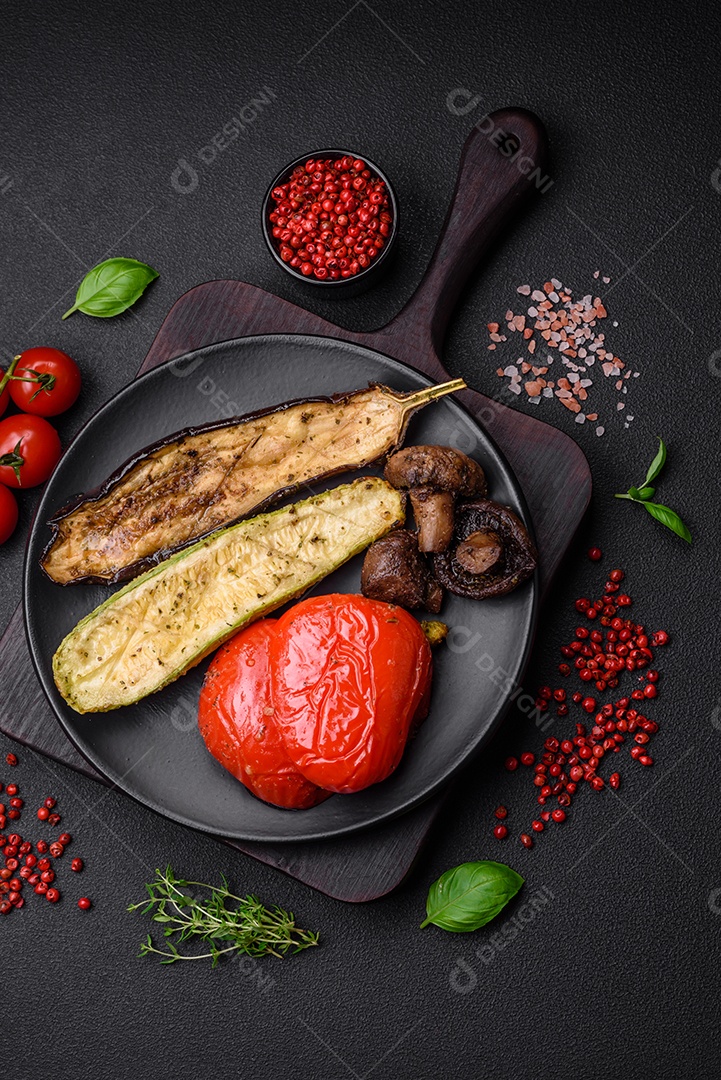 Deliciosos legumes grelhados, abobrinha, berinjela, pimentão e cogumelos com sal, especiarias e ervas sobre um fundo escuro de concreto