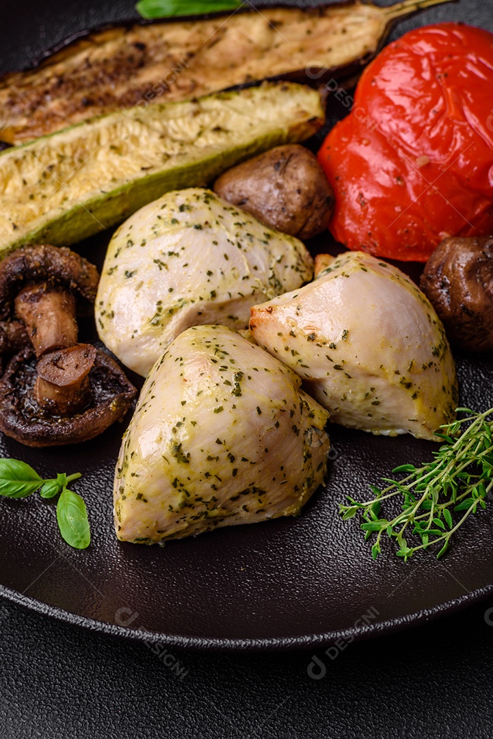 Delicioso suculento frango grelhado com sal, especiarias e ervas com legumes em um fundo escuro de concreto