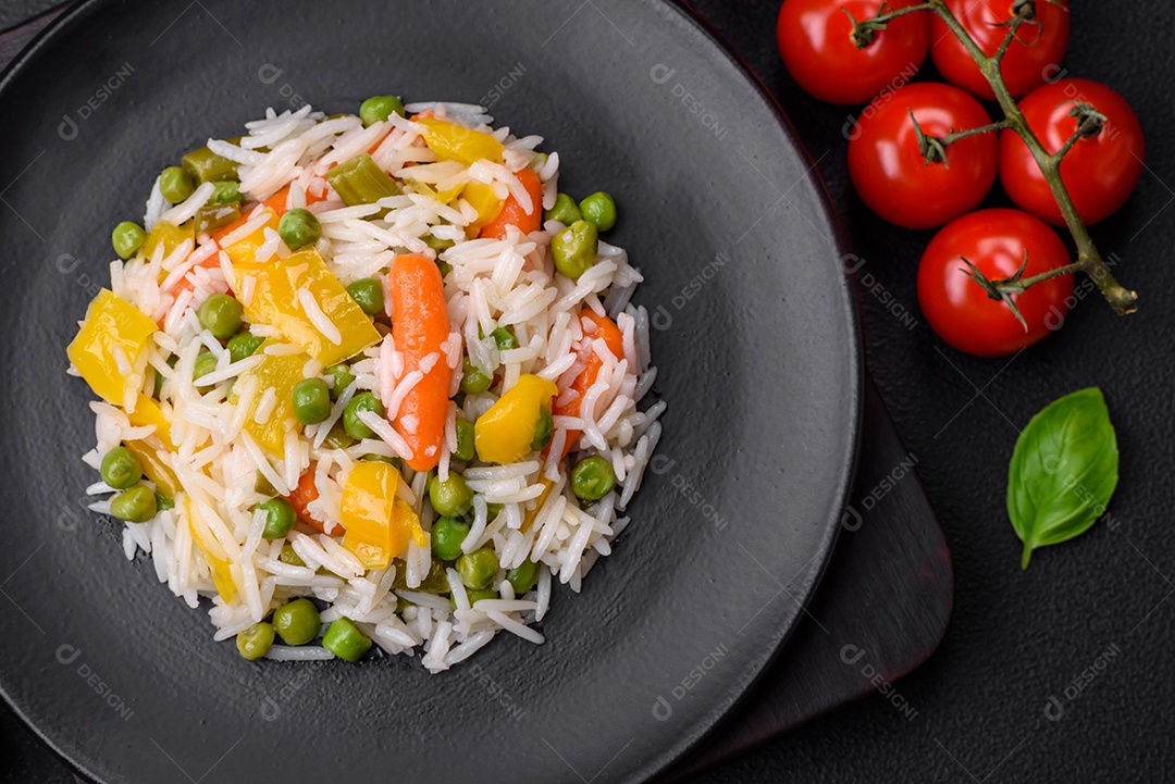 Delicioso arroz cozido branco fresco com vegetais cenouras, pimentões e feijões de espargos em uma placa cerâmica sobre um fundo escuro de concreto