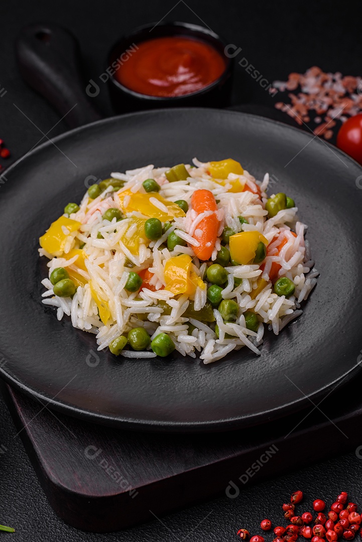 Delicioso arroz cozido branco fresco com vegetais cenouras, pimentões e feijões de espargos em uma placa cerâmica sobre um fundo escuro de concreto