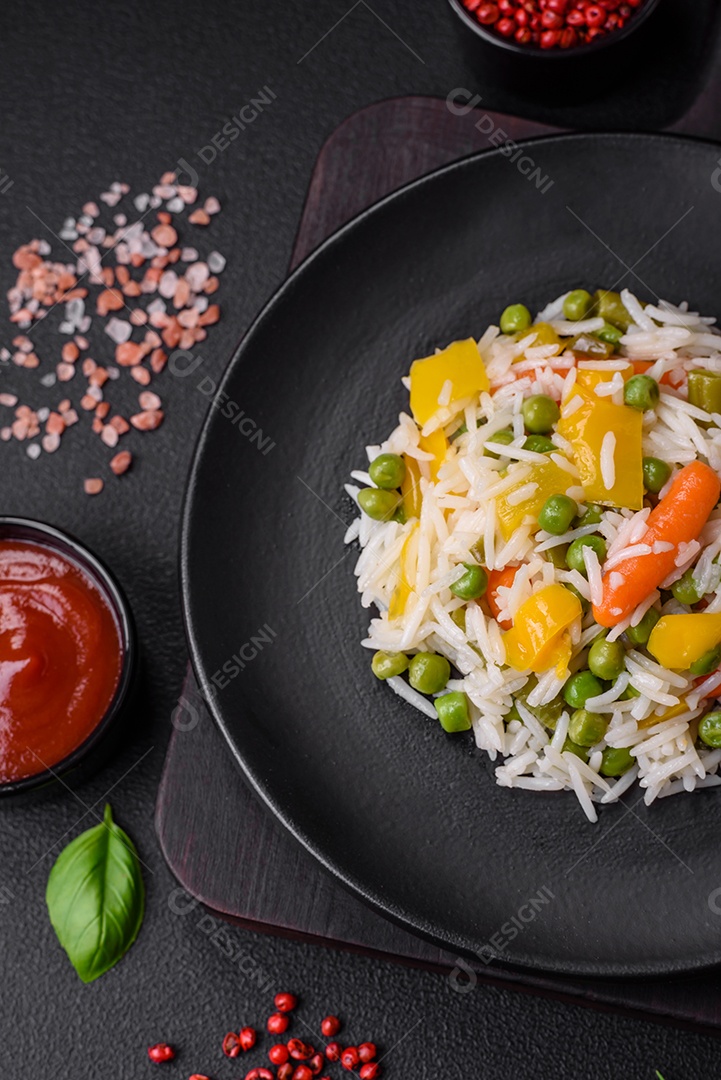 Delicioso arroz cozido branco fresco com vegetais cenouras, pimentões e feijões de espargos em uma placa cerâmica sobre um fundo escuro de concreto