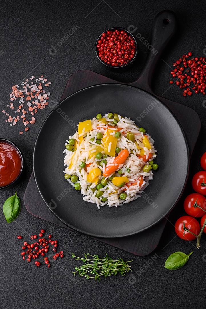 Delicioso arroz cozido branco fresco com vegetais cenouras, pimentões e feijões de espargos em uma placa cerâmica sobre um fundo escuro de concreto