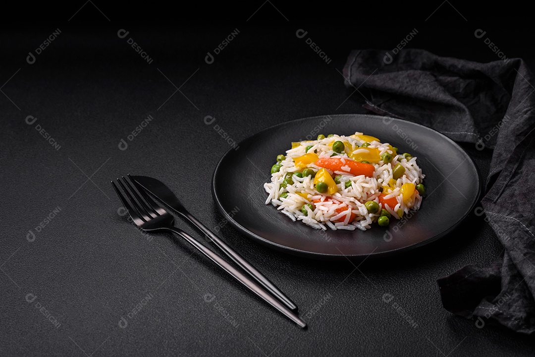 Delicioso arroz cozido branco fresco com vegetais cenouras, pimentões e feijões de espargos em uma placa cerâmica sobre um fundo escuro de concreto