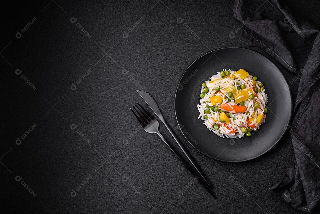 Delicioso arroz cozido branco fresco com vegetais cenouras, pimentões e feijões de espargos em uma placa cerâmica sobre um fundo escuro de concreto