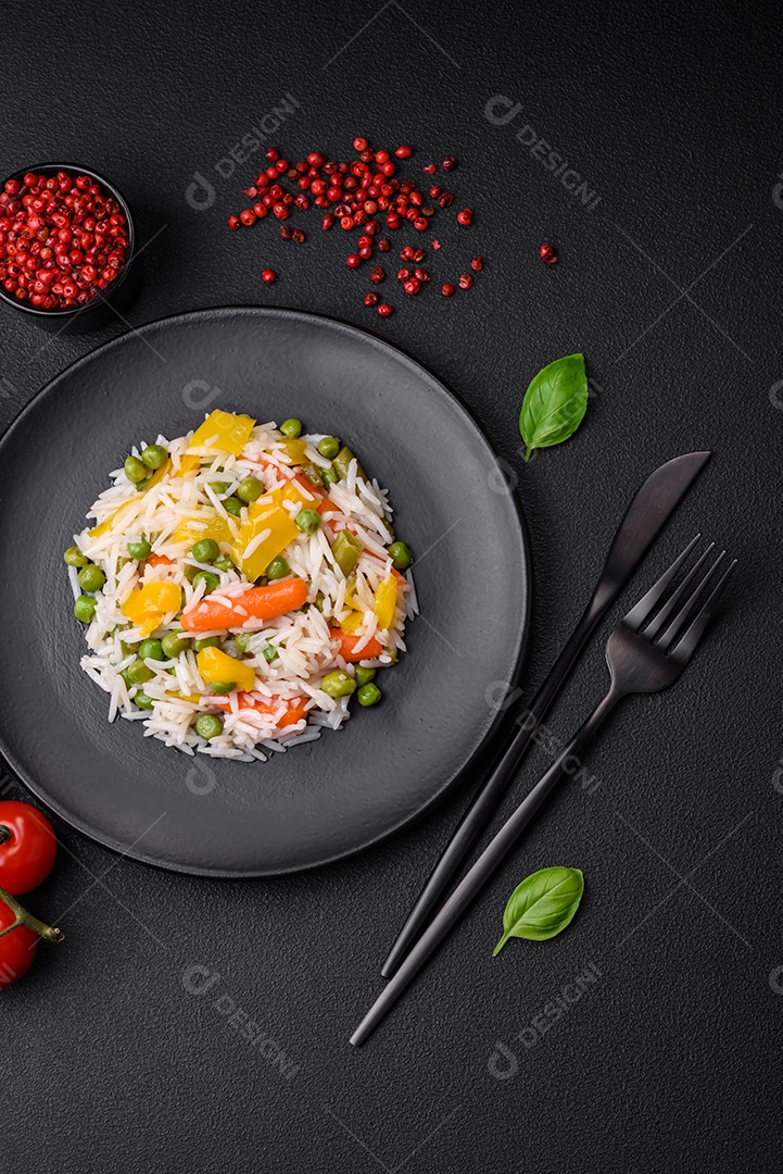Delicioso arroz cozido branco fresco com vegetais cenouras, pimentões e feijões de espargos em uma placa cerâmica sobre um fundo escuro de concreto