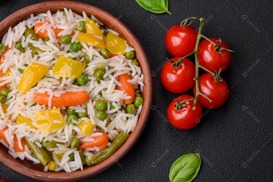 Delicioso arroz cozido branco fresco com vegetais cenouras, pimentões e feijões de espargos em uma placa cerâmica sobre um fundo escuro de concreto