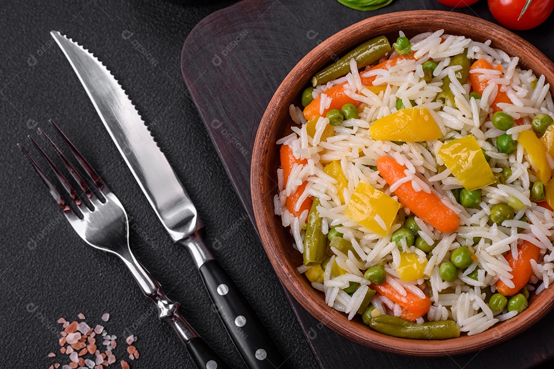 Delicioso arroz cozido branco fresco com vegetais cenouras, pimentões e feijões de espargos em uma placa cerâmica sobre um fundo escuro de concreto