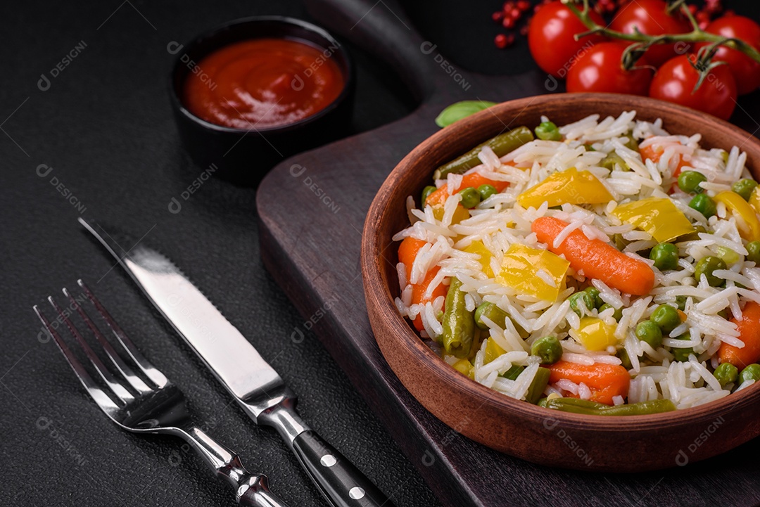 Delicioso arroz cozido branco fresco com vegetais cenouras, pimentões e feijões de espargos em uma placa cerâmica sobre um fundo escuro de concreto